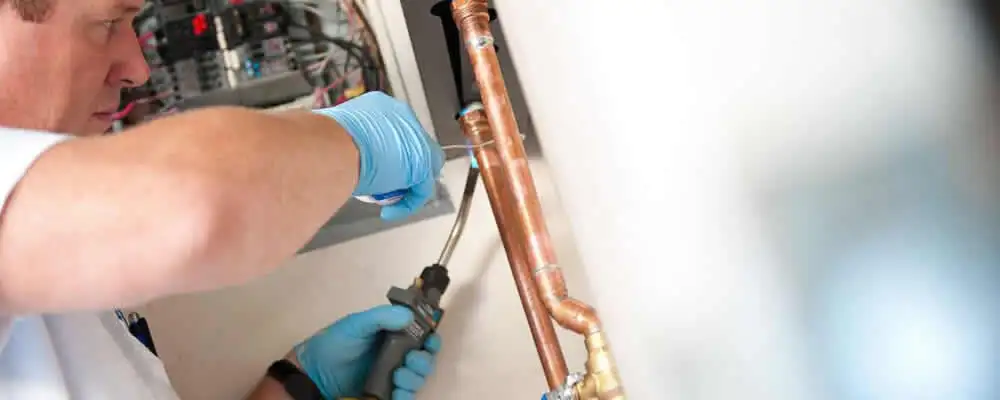 Water heater repair technician testing copper pipe connections and controls in San Mateo, CA